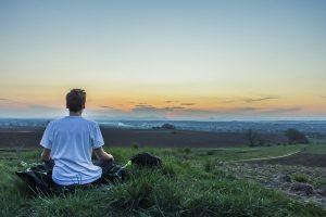 A guy meditating on a meadow.