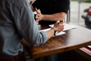 Two men sitting at a wooden table, explaining something