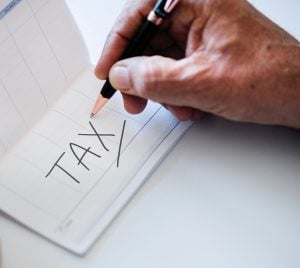 A man writing and underlining a word 'tax' on a piece of paper