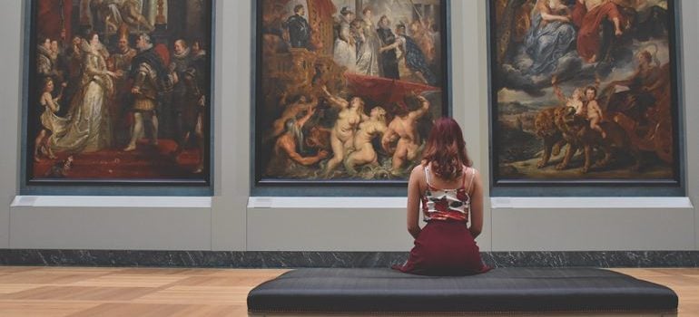 A girl sitting in front of three renaissance pictures in a gallery.