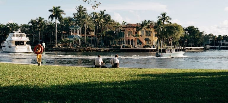 People sitting on grass near boats and palm trees after moving to Fort Lauderdale
