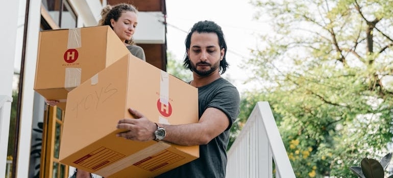 A couple carrying boxes on steps while moving out of house