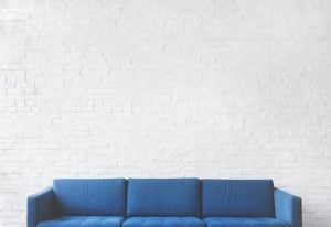 Blue couch in front of a white brick wall