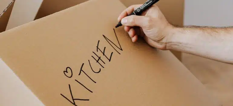 A man writing the word kitchen on a cardboard box 