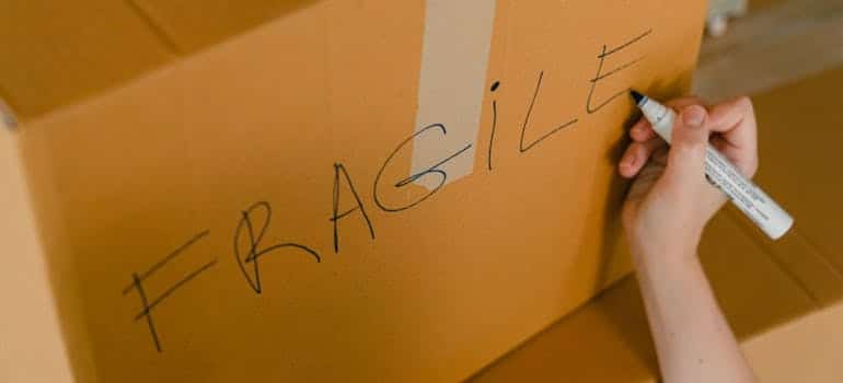 A person labels a box fragile after they efficiently pack fragile items