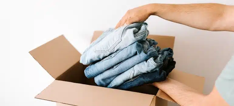 A person packing jeans into cardboard box for storage