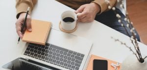 person holding a mug next to a laptop on a desk