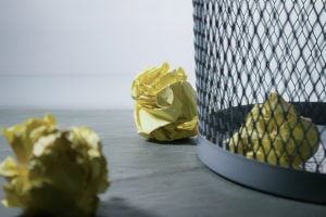 Protect your personal information by destroying all the old documents. A crumpled yellow paper inside and outside the garbage bin, a close-up photo of the bin