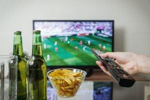 person watching a football match on tv with two beer bottles and a bowl of chips