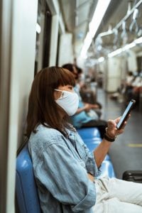 Picture of a woman on a train, wearing a mask. Having a home office means that you don't have to lose time and risk your health in public commute.