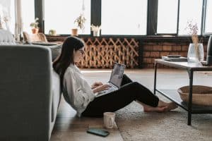 A woman sitting on the floor doing one of the best things to do in Miami in the fall which is to enjoy an online book fair.