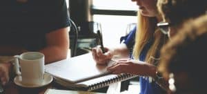 a woman writing something down in her notes as she talks with other employees