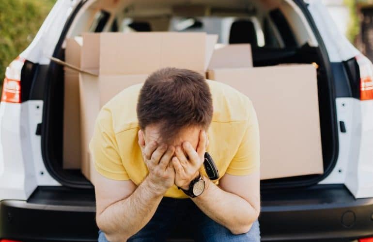 A man sitting at the back of his car, loaded with moving boxes.