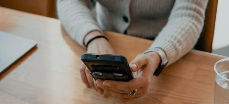 A woman sitting on a chair holding her phone in her hands searching for the best time to move a hotel