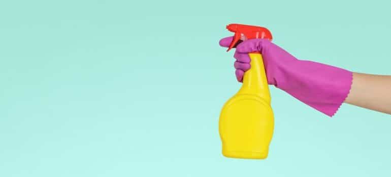 A hand with a glove in hand holds a cleaning spray 