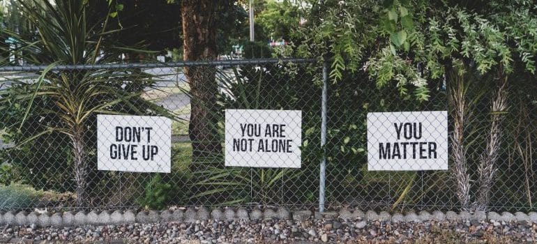 Three quotes are written on paper, hanging on a fence