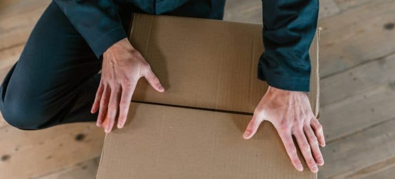 man in dark green jumpsuit holding his hands on the paper box