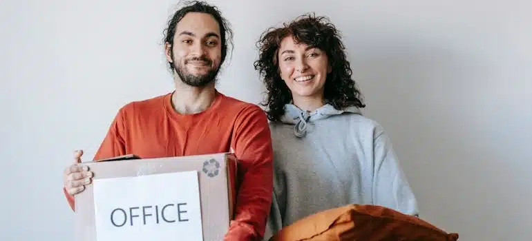 Two smiling employees holding office boxes know what to throw away before office move