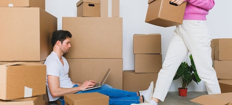 A man sitting amid boxes browsing on his laptop how to declutter office for a move
