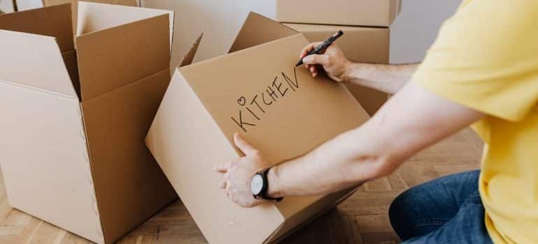 Man writing the word kitchen on a moving box with a marker
