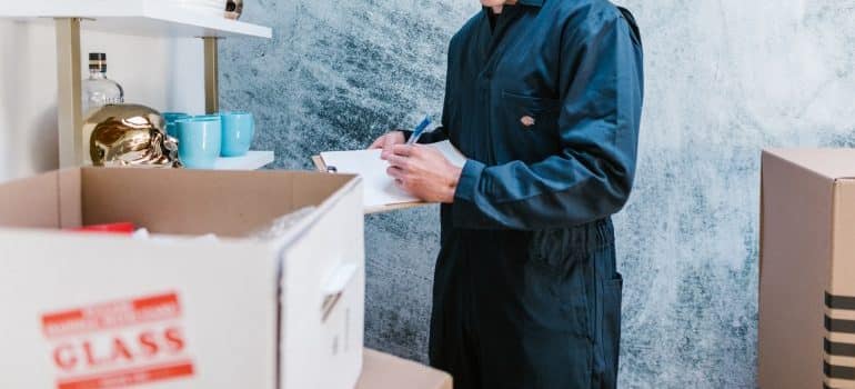 Man standing beside moving boxes and writing