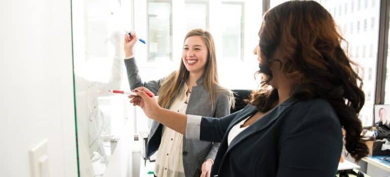 Two women writing on a white board 