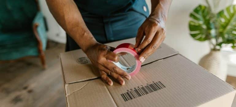 A man closing a box with a duck tape - move office furniture to Bal Harbour