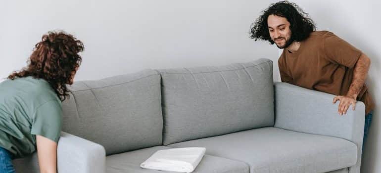 A woman and a man lifting and moving a sofa