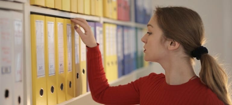 A woman looking over yellow document binders on a shelf
