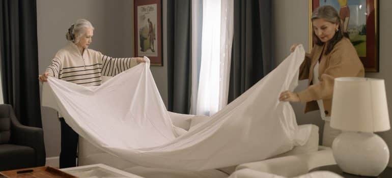 Two women are covering the couch with a blanket