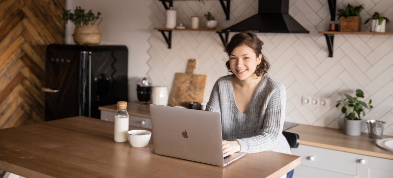 a smiling woman working on her laptop thinking about benefits of renting storage before having a baby