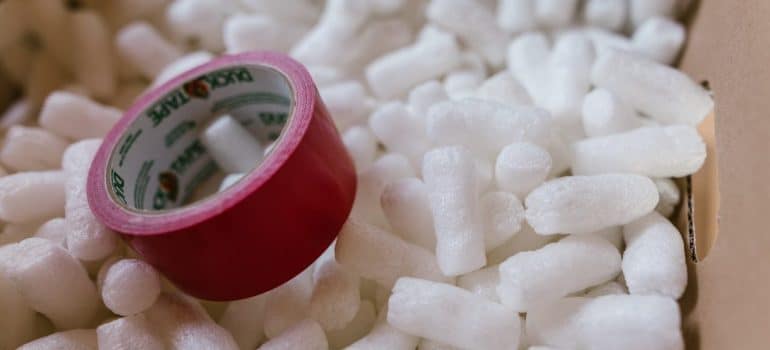 a red packing tape inside a cardboard box full of packing peanuts to pack porcelain when moving long distance