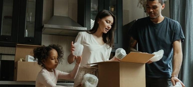 parents unpacking a box in the kitchen with their daugther