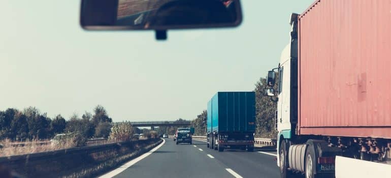 A picture taken from a vehicle with a road ahead and a moving trucks in front of the vehicle.