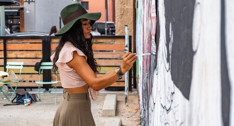 a woman wearing a green hat drawing a mural on a wall