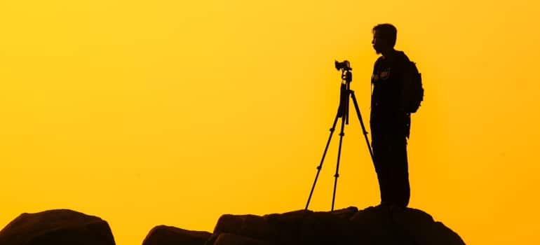 a man standing on a rock with a camera , in front of a yellow background