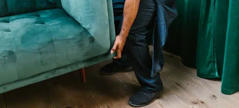 A man putting down the green sofa he is carrying