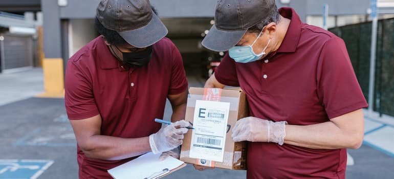 Two men are writting something on a box.