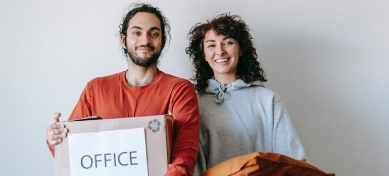 a man and a woman holding some pillows and a cardboard box with office materials