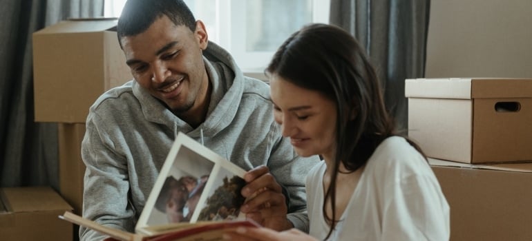 a woman and a man looking at photo albums, surrounded by packed boxes