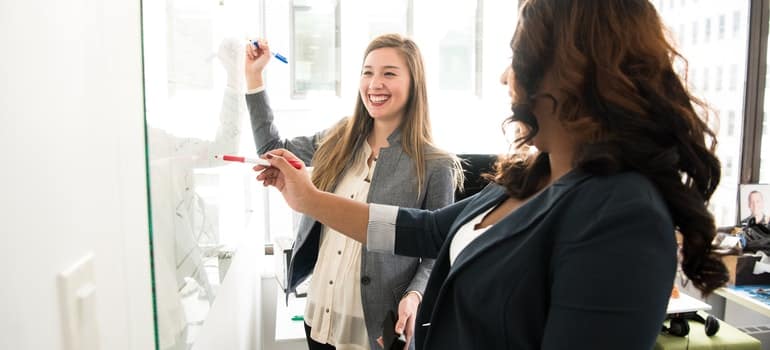 Two women are writting on a board.