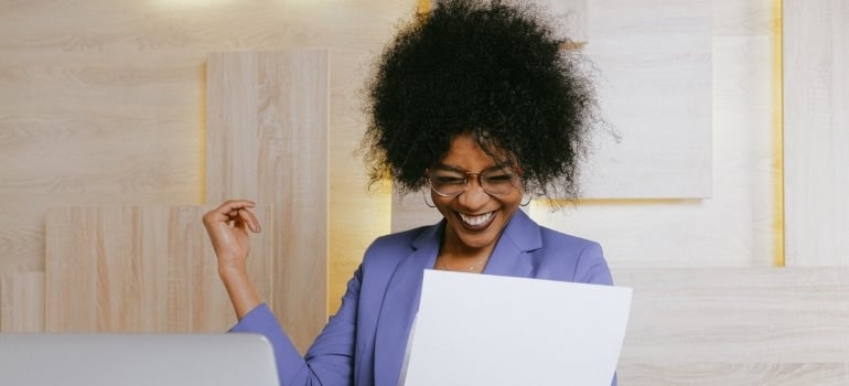 a woman smiling while looking at a piece of paper and a laptop in an office