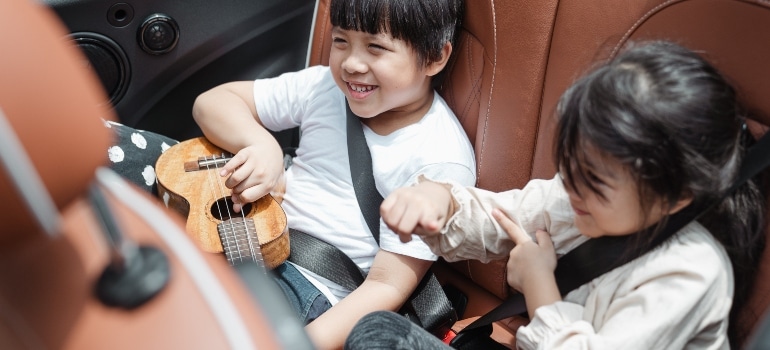 kids playing in car with their toys which are on the list of items to keep at hand on moving day