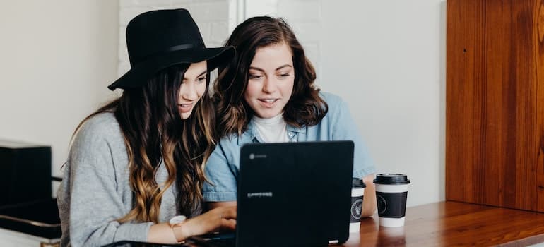 Two women near a table using a laptop looking how to speed up relocation in Fort Lauderdale