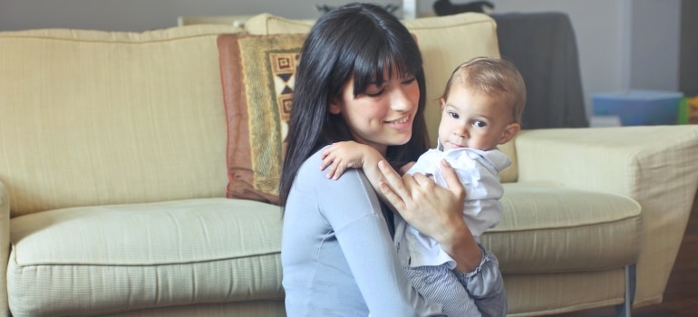 Happy woman is holding a baby after she managed to unpack after moving to North Miami with a baby