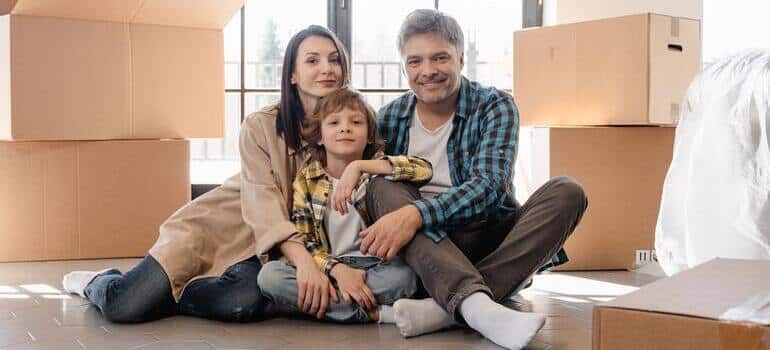 family with young kid is sitting between moving boxes