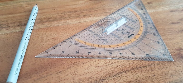 Gray pencil and triangular ruler on brown wooden surfance that people often use to measure the sizes of their furniture and appliances after relocation.