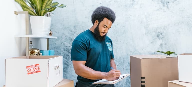 A man in a blue shirt from a local moving company writing something down on a paper, as he had been hired to arrange furniture and appliances after relocation.