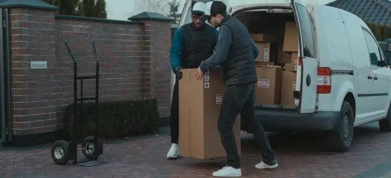 two movers handling a large cardboard box and placing it onto a hand truck