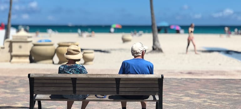 Two senior citizens sitting on a benach close to the beach while thinking about the most popular cities for relocation in Broward County;